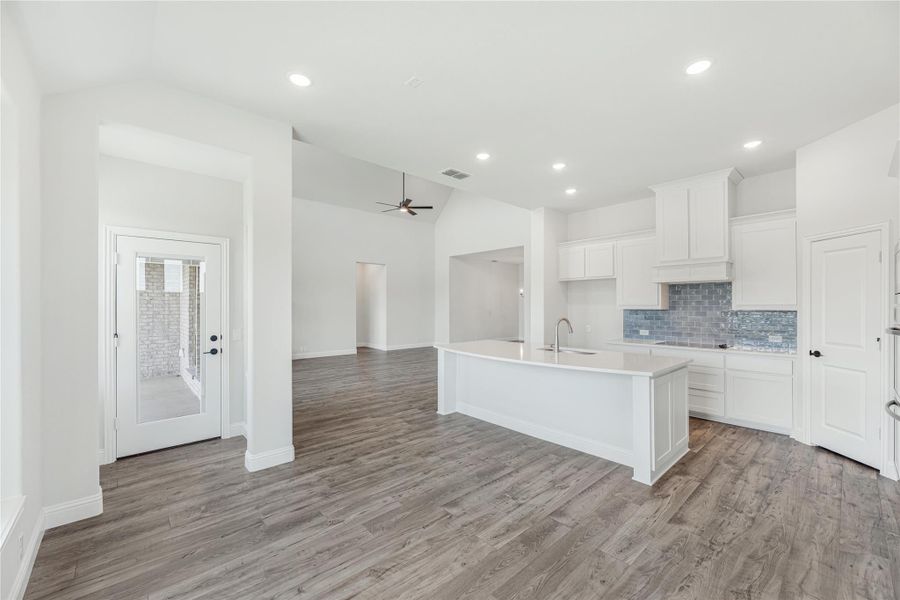 Open kitchen with white cabinets, center island, blue tile backsplash, and wood floors open to living area
