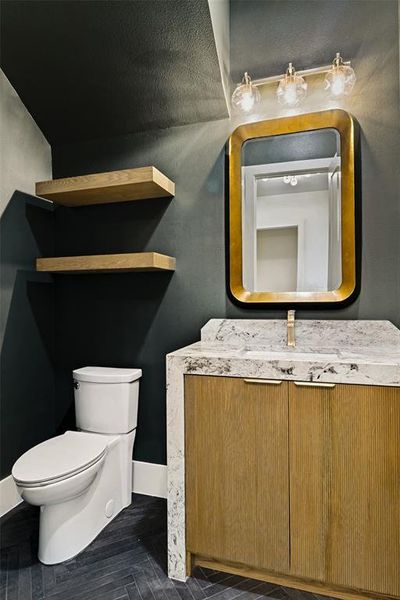 Bathroom featuring a wood-finish vanity with a stone countertop, a gold-framed mirror, and a three-light vanity fixture Bathroom featuring a wood-finish vanity with a stone countertop, a gold-framed mirror, and a three-light vanity fixture