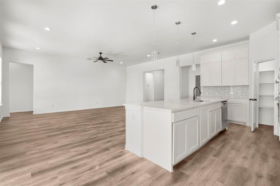 Kitchen featuring ceiling fan, a kitchen island with sink, pendant lighting, decorative backsplash, and white cabinets