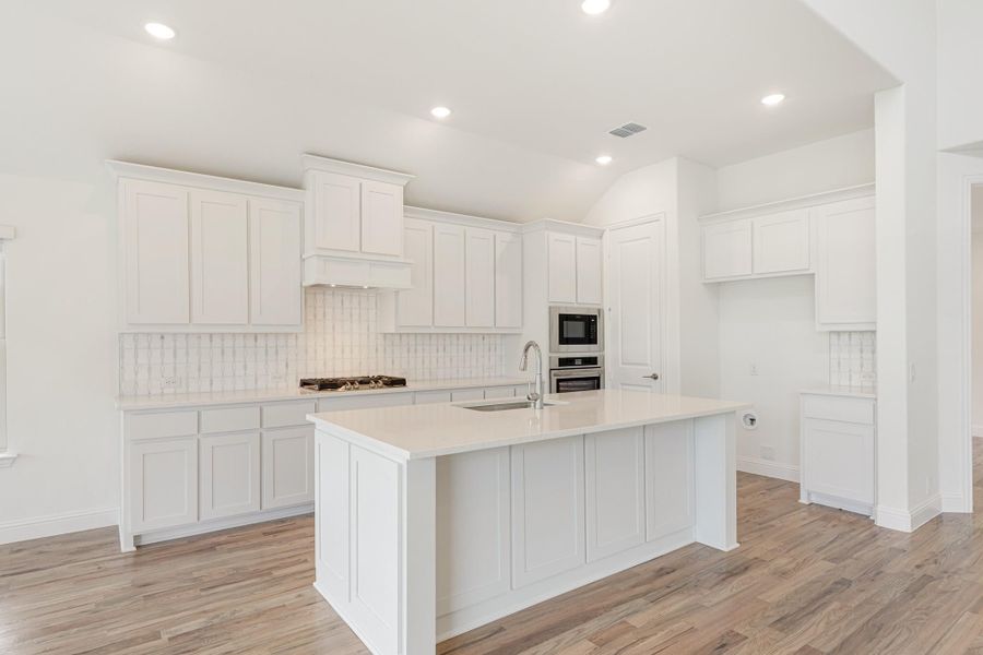White kitchen with large center island, white quartz countertops, stainless steel appliances, and wood-look floors White kitchen with large center island, white quartz countertops, stainless steel appliances, and wood-look floors