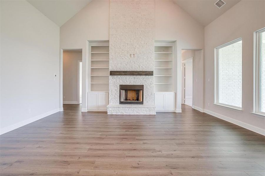 Unfurnished living room with wood-type flooring, a stone fireplace, built in features, and high vaulted ceiling