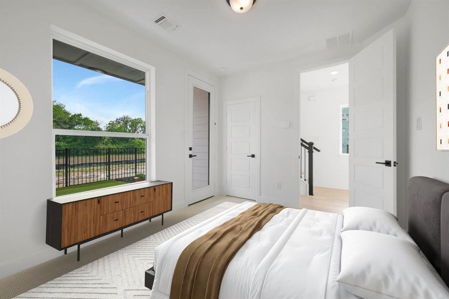 Spacious bedroom featuring a large window, a built-in wood-finish cabinet with a light-colored countertop, and a white paneled door with matte black hardware