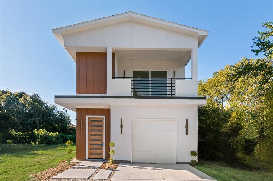 Modern home featuring a balcony, a garage, a front yard, stucco siding, and concrete driveway Modern home featuring a balcony, a garage, a front yard, stucco siding, and concrete driveway