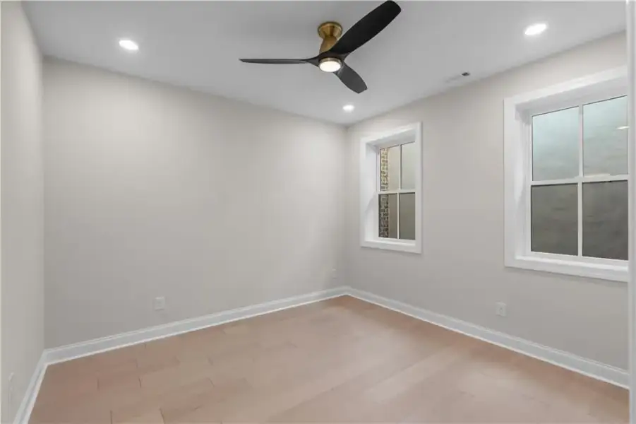 Recessed lighting, light-toned wood-finish flooring, white trim, two windows, and a ceiling fan with integrated lighting