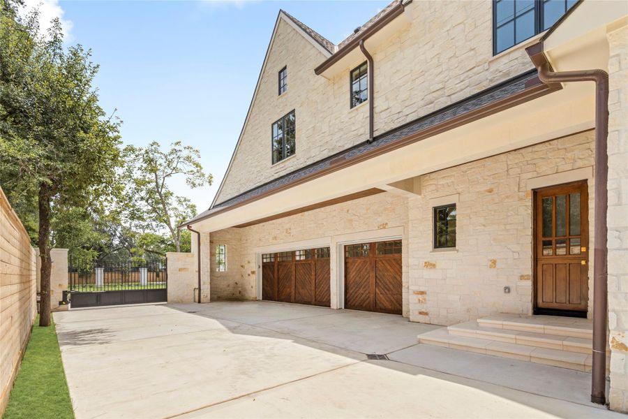 The private motor court provides gated access to the three-car garage, with custom wood garage doors that complement the home’s architecture. A deep covered overhang adds shelter while giving this secondary arrival area a polished, thoughtfully designed feel. The private motor court provides gated access to the three-car garage, with custom wood garage doors that complement the home’s architecture. A deep covered overhang adds shelter while giving this secondary arrival area a polished, thoughtfully designed feel.