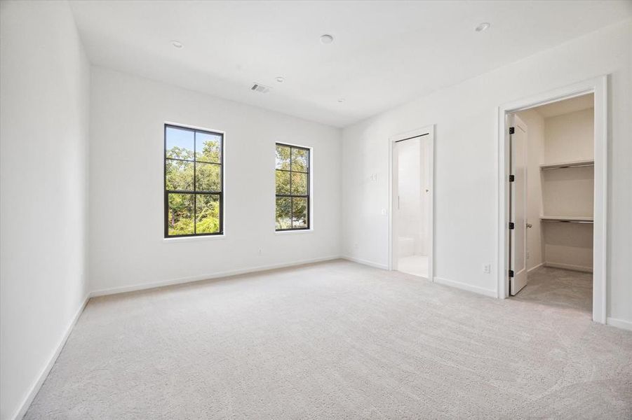 This secondary bedroom features soft carpeting, adding comfort underfoot, with two large windows that provide plenty of natural light. The room includes a large walk-in closet and an ensuite bathroom, making it both functional and private.