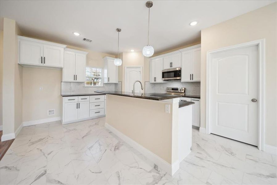 Kitchen featuring white cabinetry, hanging light fixtures, backsplash, a center island with sink, and appliances with stainless steel finishes