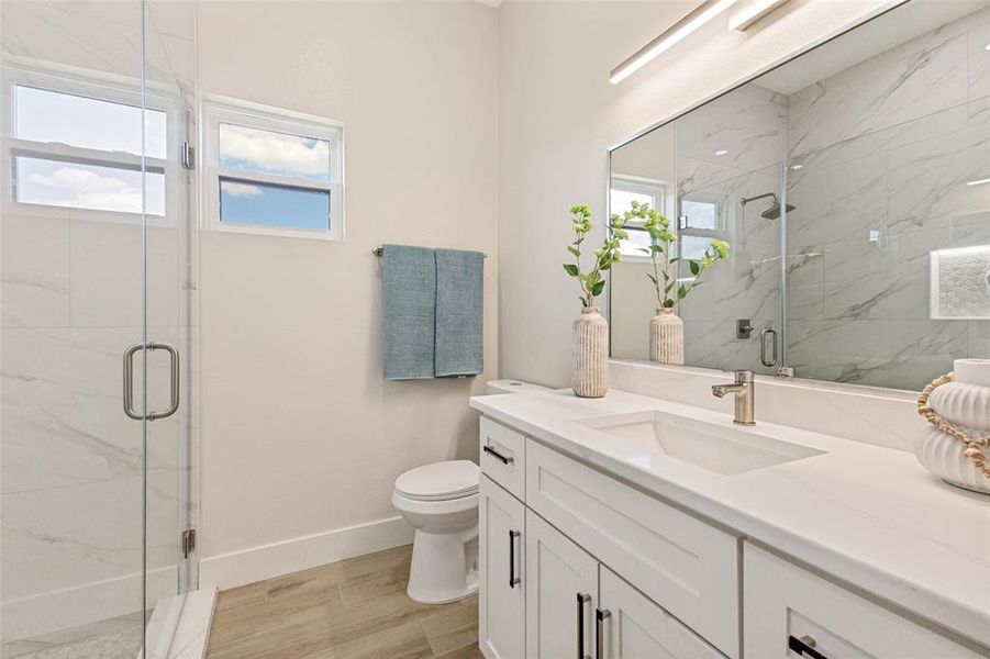 Contemporary bathroom featuring a spacious glass-enclosed shower, dual windows, a floating vanity with a single basin, a large wall-mounted mirror, and wood-finish flooring