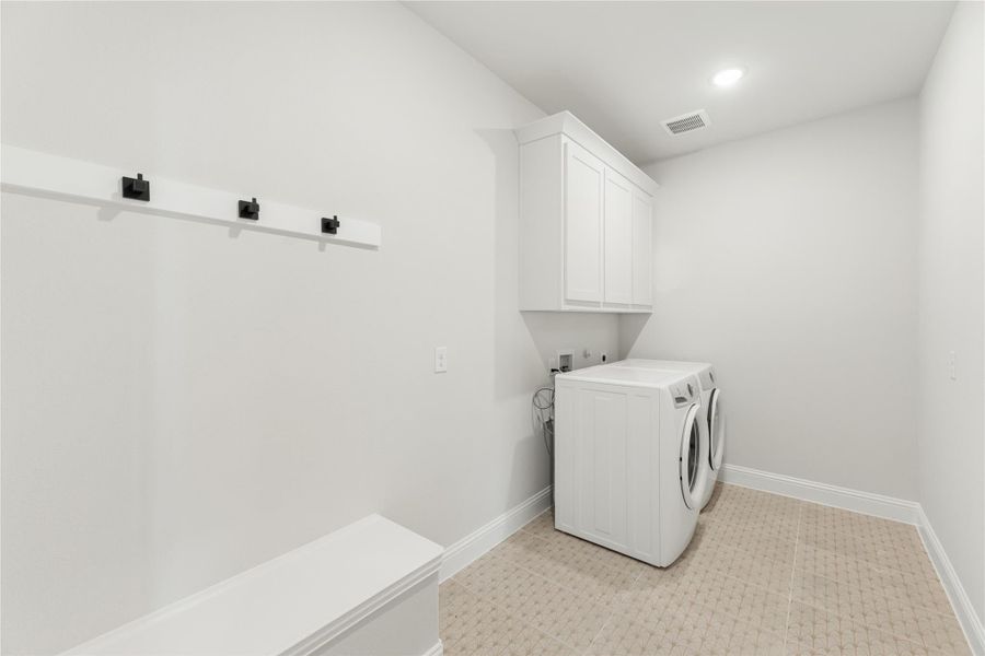 Laundry room with washer and dryer, white upper cabinets, wall hooks, and tile floor