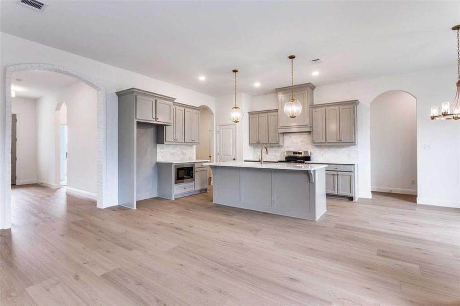 Kitchen with stainless steel electric range oven, decorative light fixtures, black microwave, gray cabinetry, and a kitchen island with sink