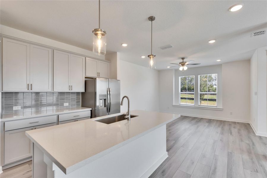 Kitchen with tasteful backsplash, stainless steel fridge with ice dispenser, hanging light fixtures, light wood-style flooring, and light stone counters