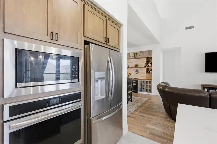 Kitchen appliances featuring stainless steel built-in microwave and oven, a stainless steel refrigerator, and light wood-finish cabinetry