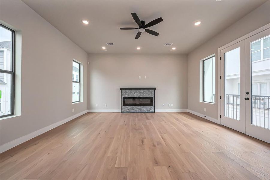 Discover a bright, spacious living room with elegant hardwood floors, a sleek modern fireplace, and expansive windows. Enjoy the comfort of a ceiling fan and recessed lighting. French doors lead to a balcony, perfect for seamless indoor-outdoor living.