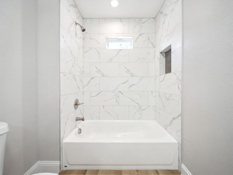 Bathroom featuring hardwood / wood-style flooring, tiled shower / bath combo, and toilet