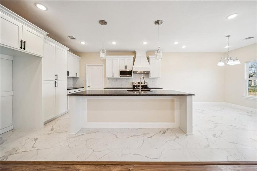 Kitchen with sink, white cabinetry, hanging light fixtures, and an island with sink