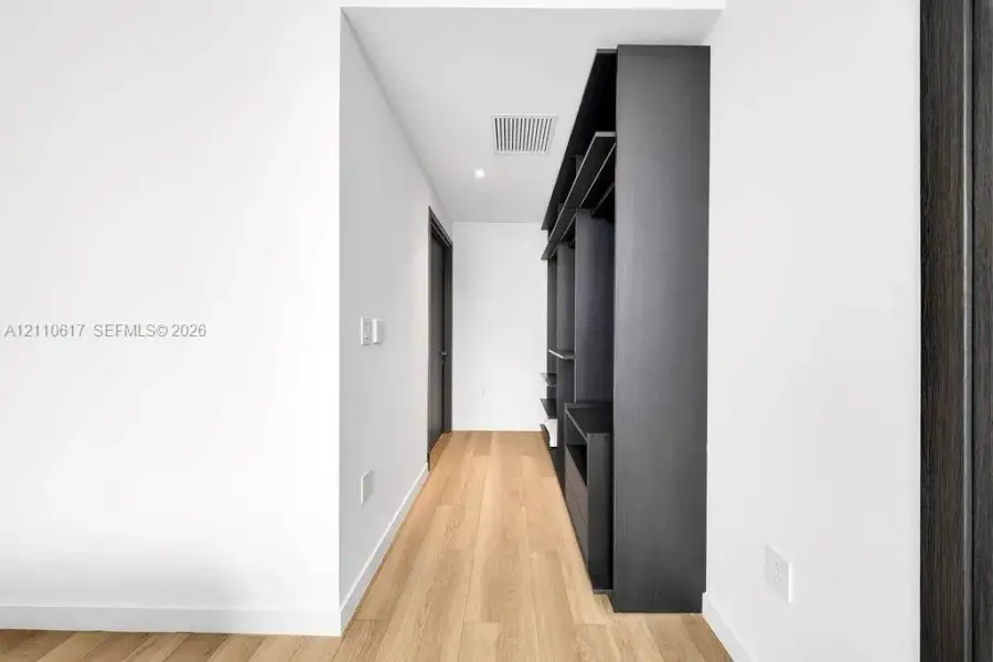 Hallway featuring wood-finish flooring, recessed ceiling lighting, and built-in dark cabinetry with open shelving Hallway featuring wood-finish flooring, recessed ceiling lighting, and built-in dark cabinetry with open shelving