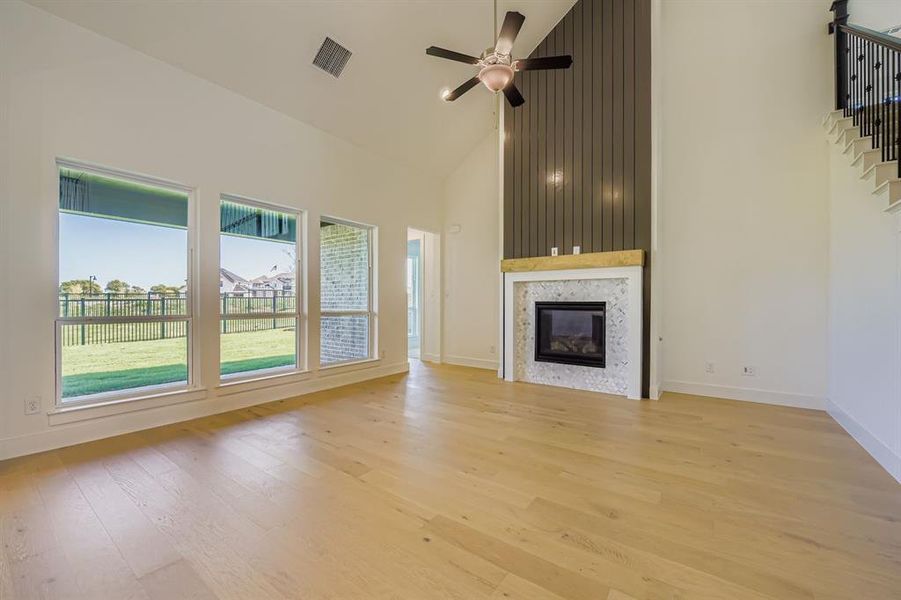 Unfurnished living room featuring high vaulted ceiling, light wood finished floors, a fireplace, and ceiling fan