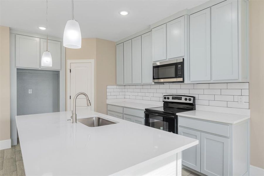 Kitchen featuring sink, hanging light fixtures, stainless steel appliances, a center island with sink, and light wood-type flooring