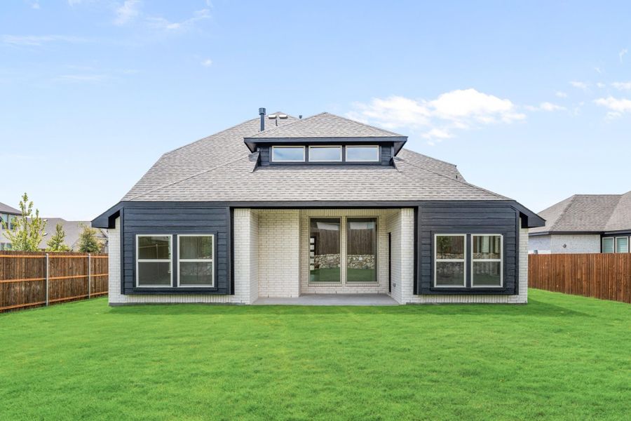 Rear exterior of home with dark siding, white brick, covered patio, and fenced backyard with green lawn