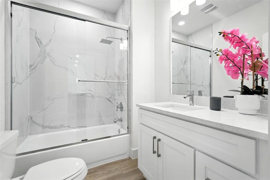 Bathroom featuring enclosed tub / shower combo, vanity, and light wood-style flooring