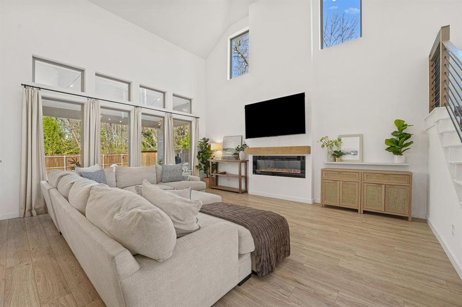 Living room with a glass covered fireplace, light wood-style floors, healthy amount of natural light, and high vaulted ceiling