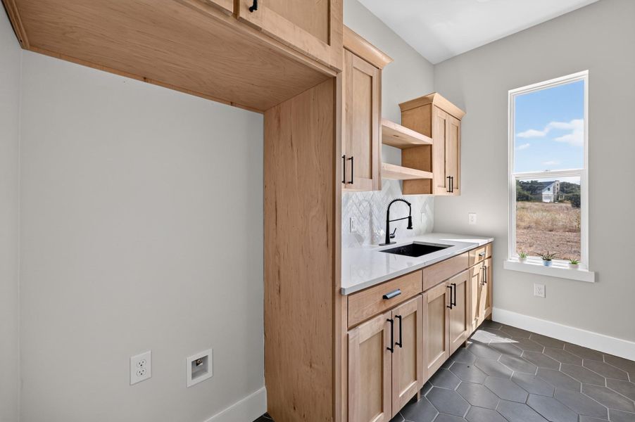 Natural wood cabinetry and dark hexagonal floor tiles define this functional utility space.