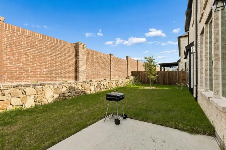 Private backyard featuring a concrete patio, green lawn, and a mature tree