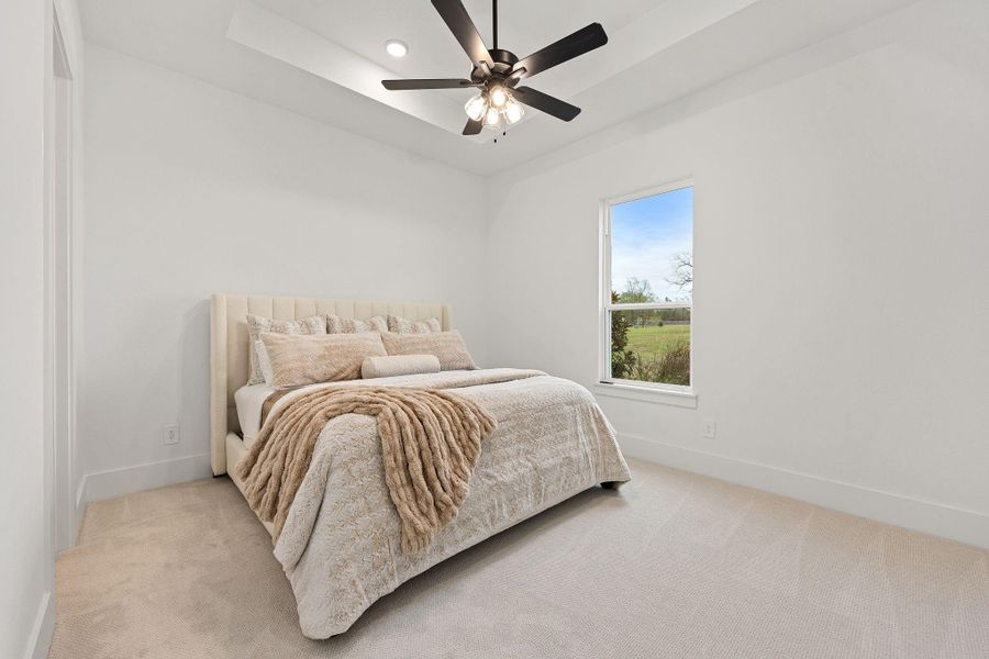 This cozy bedroom features a plush bed with neutral bedding, a ceiling fan, and a large window offering a view of the outdoors, creating a bright and inviting space. The bedroom is located downstairs with its own en-suite bathroom.