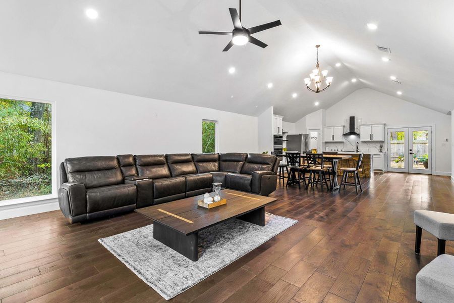 This spacious open-concept living area features high vaulted ceilings, a modern kitchen with stainless steel appliances, and elegant hardwood floors. Natural light streams in through large windows, enhancing the airy feel. The room includes a stylish lighting fixtures, creating a perfect blend of comfort and contemporary design.