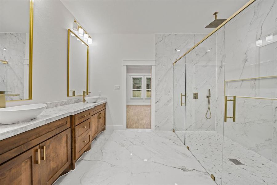 Spacious bathroom featuring a dual vanity with wood cabinetry and vessel sinks, a large walk-in shower with gold-finish fixtures, and marble-look tile flooring