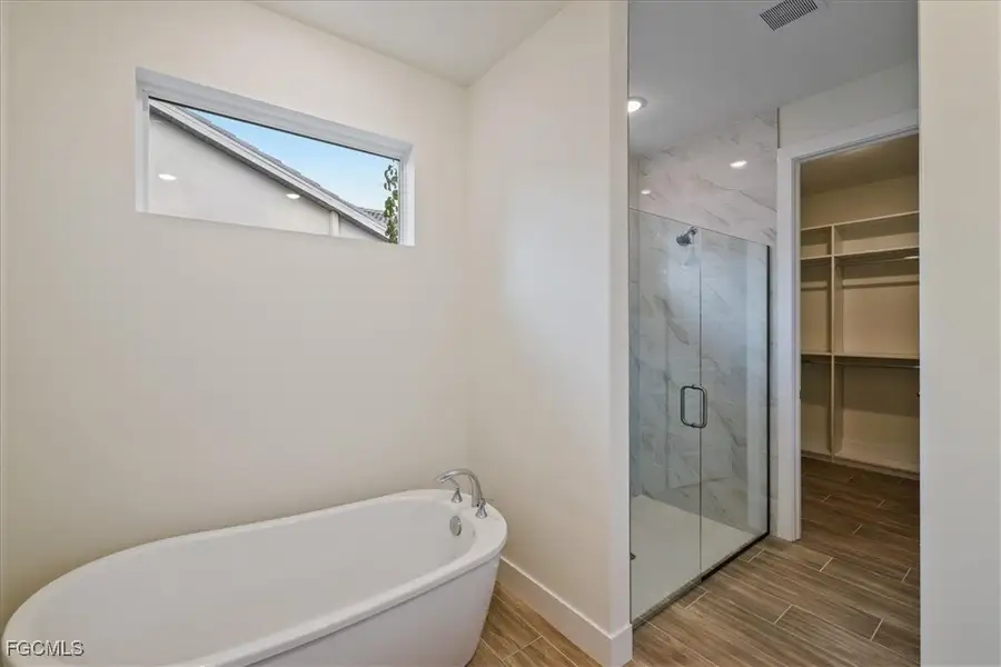 Full bath with wood tiled floors, a freestanding tub, a marble finish shower, and a spacious closet