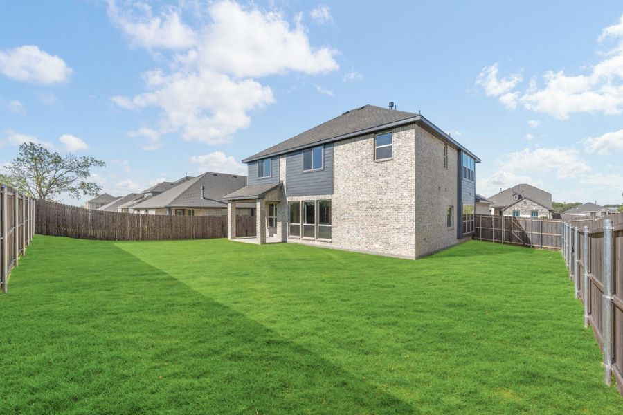 Two-story brick home with covered patio, large fenced backyard, and green lawn viewed from rear