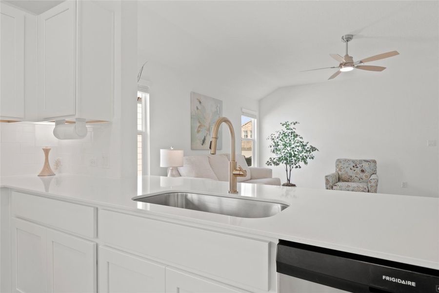 A deep stainless steel undermount sink and modern gold-tone faucet anchor the expansive granite island, offering a clear view into the living room for a truly connected lifestyle.