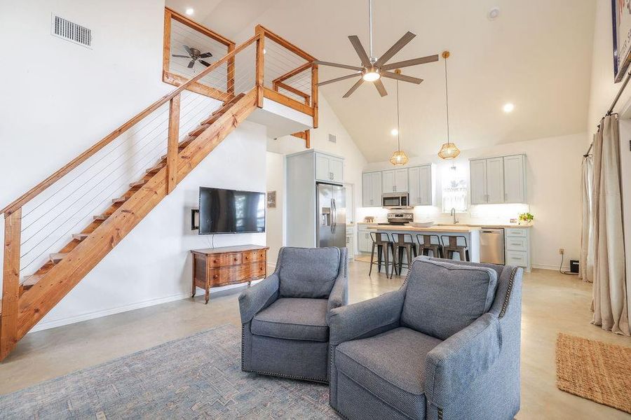 Living area with high vaulted ceiling, ceiling fan, and stairway