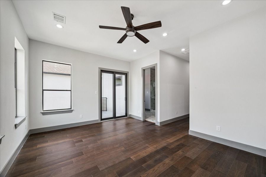 Warm wood floors and neutral finishes give this primary suite a calm, inviting atmosphere. Sliding glass doors lead to a private balcony, while direct access to the ensuite bath adds everyday convenience.