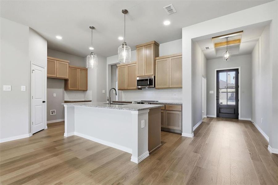 Kitchen featuring light stone counters, light wood finished floors, tasteful backsplash, a kitchen island with sink, and recessed lighting Kitchen featuring light stone counters, light wood finished floors, tasteful backsplash, a kitchen island with sink, and recessed lighting