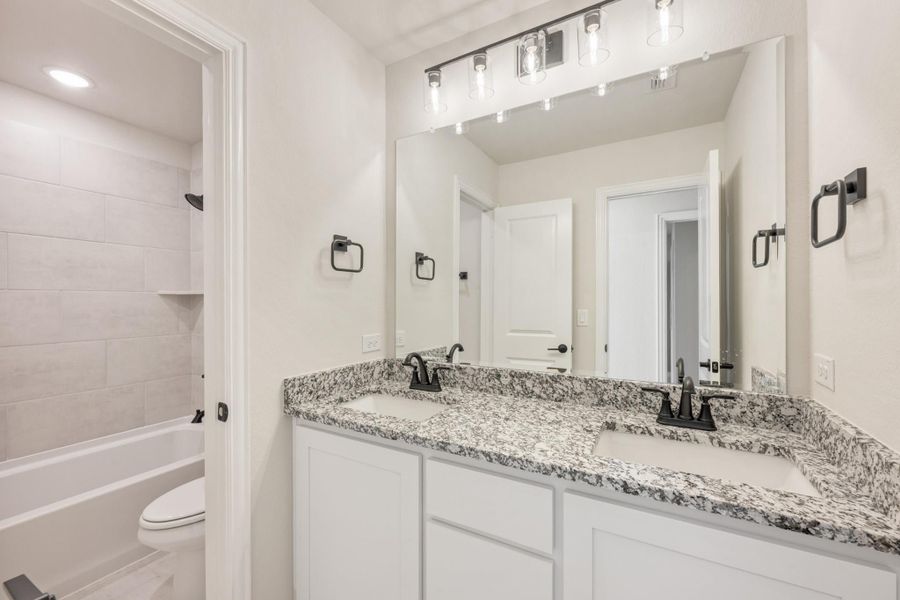 Bathroom with double sink vanity, granite countertops, white cabinets, and tiled tub-shower combo