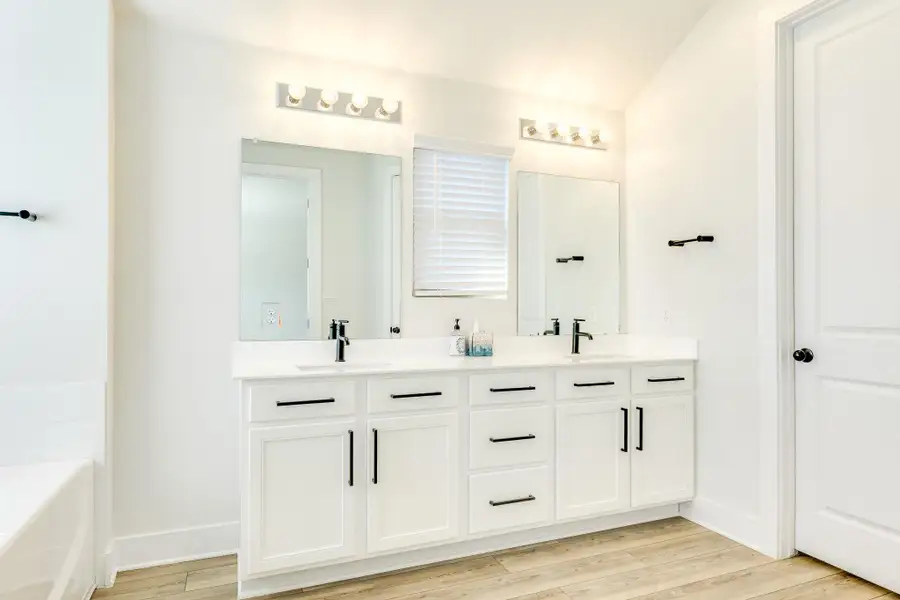 Bathroom with double vanity, a bath, and light wood-type flooring