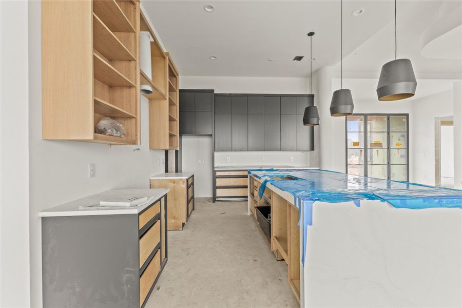 Kitchen featuring dual islands with protective covering, a trio of pendant lights, recessed ceiling lighting, light wood-finish open shelving, and dark flat-panel cabinetry