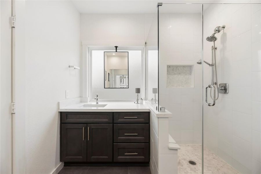 Primary bath vanity with drawer storage beside the enlarged walk-in shower and private water closet.