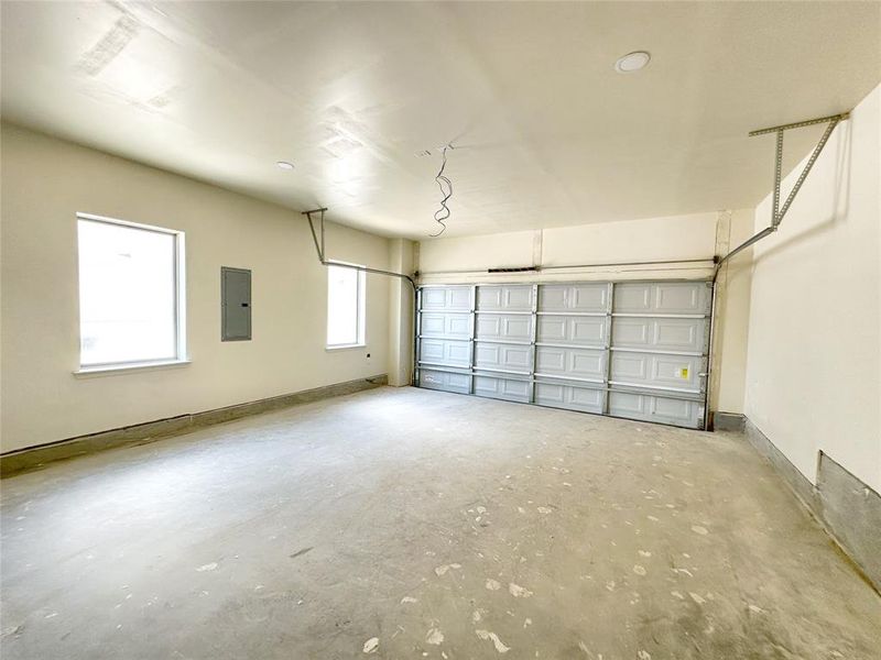 Garage featuring electric panel and baseboards