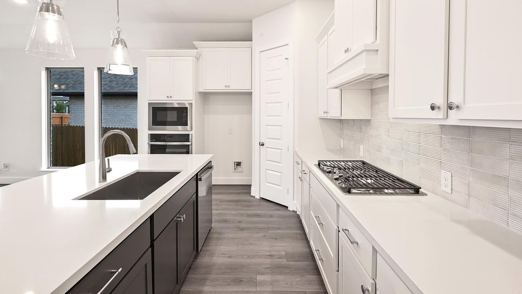 Kitchen with white cabinets, pendant lighting, light wood finished floors, appliances with stainless steel finishes, and dark cabinets Kitchen with white cabinets, pendant lighting, light wood finished floors, appliances with stainless steel finishes, and dark cabinets