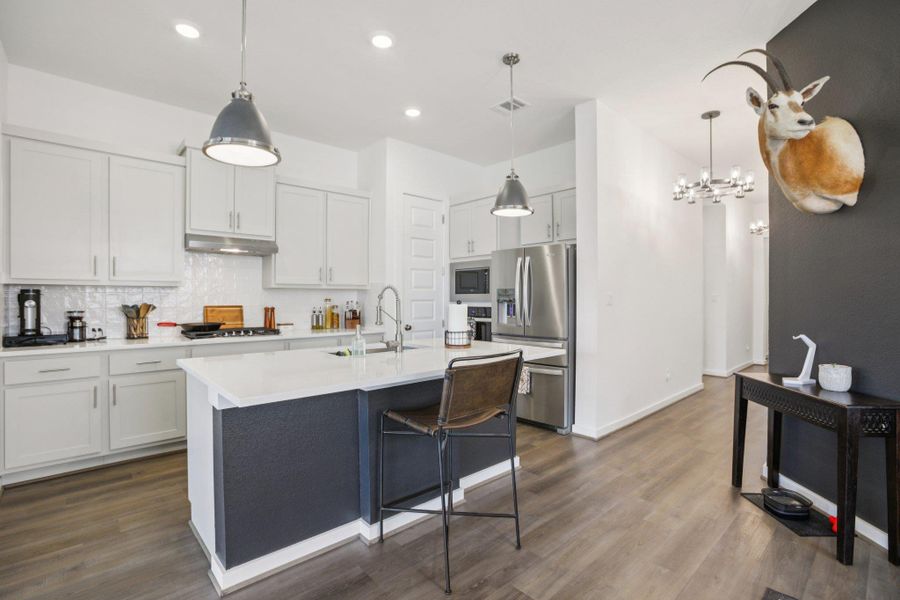 Kitchen featuring decorative backsplash, hanging light fixtures, a breakfast bar area, appliances with stainless steel finishes, and dark wood-style floors Kitchen featuring decorative backsplash, hanging light fixtures, a breakfast bar area, appliances with stainless steel finishes, and dark wood-style floors