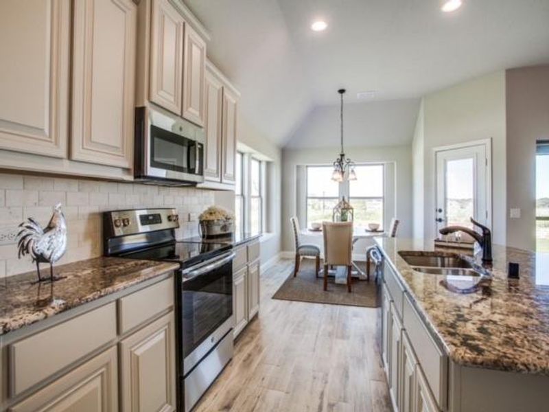 Kitchen featuring appliances with stainless steel finishes, dark stone counters, a chandelier, light wood finished floors, and pendant lighting