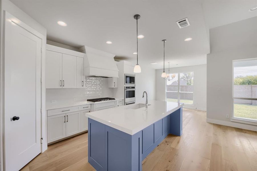 Spacious kitchen featuring a large central island with an integrated sink, crisp white cabinetry, built-in stainless steel appliances, and wood-finish flooring