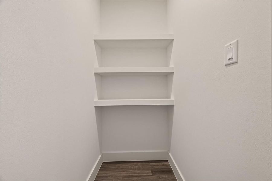 This photo shows closet with three built-in white shelves and a light switch on the right wall. The space has clean white walls and a wood-look floor. This photo shows closet with three built-in white shelves and a light switch on the right wall. The space has clean white walls and a wood-look floor.