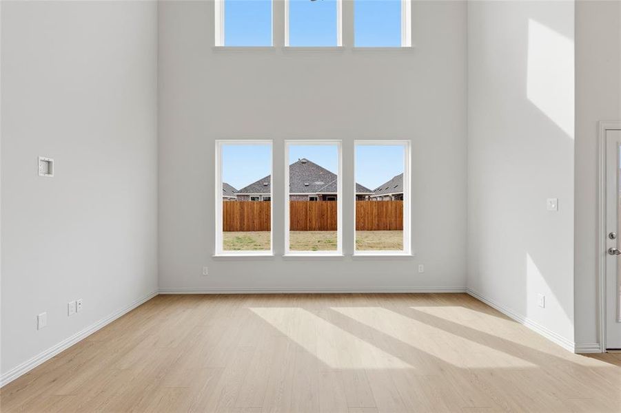 Spare room featuring healthy amount of natural light, light wood-type flooring, and a high ceiling