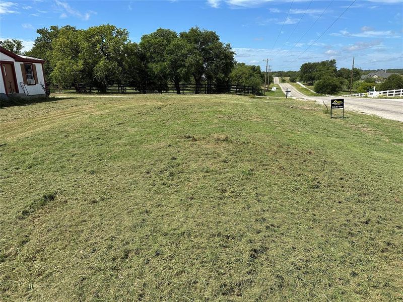 Expansive grassy lot featuring mature trees, a paved roadway, and a white split-rail fence Expansive grassy lot featuring mature trees, a paved roadway, and a white split-rail fence