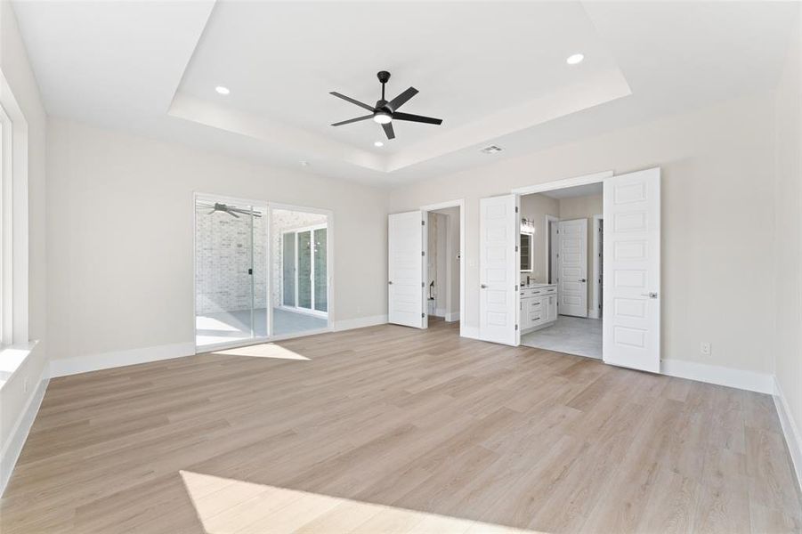 Unfurnished bedroom featuring light wood-type flooring, access to outside, a tray ceiling, ceiling fan, and recessed lighting Unfurnished bedroom featuring light wood-type flooring, access to outside, a tray ceiling, ceiling fan, and recessed lighting