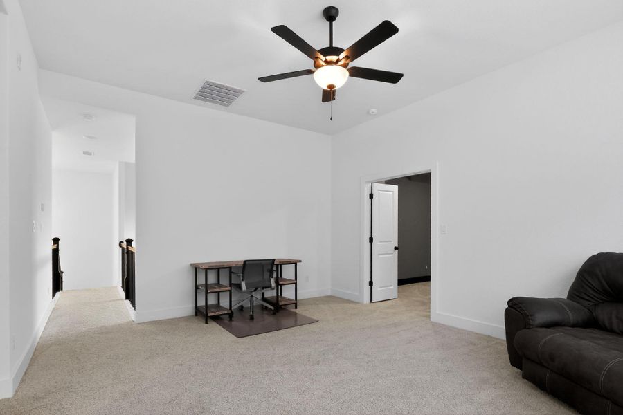 Carpeted bonus room with a ceiling fan light fixture, an open doorway, and a hallway with dark wood railings Carpeted bonus room with a ceiling fan light fixture, an open doorway, and a hallway with dark wood railings
